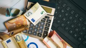 Euro-Banknoten, Laptop und Haushaltsbudget als Symbol für finanzielle Belastung trotz Arbeit