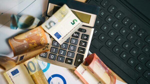 Euro-Banknoten, Laptop und Haushaltsbudget als Symbol für finanzielle Belastung trotz Arbeit