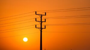 Stromleitungen vor orangefarbenem Himmel als Symbol für Stromausfall und Hitze