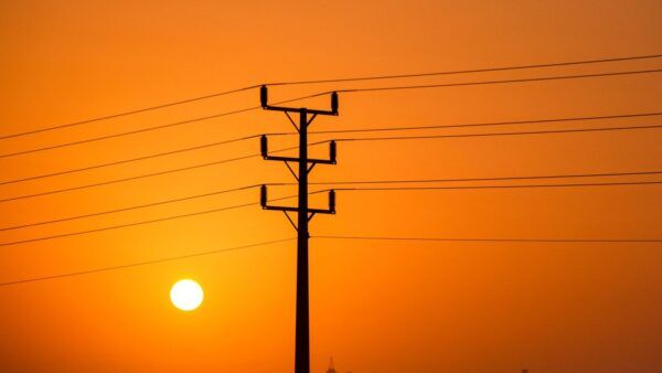 Stromleitungen vor orangefarbenem Himmel als Symbol für Stromausfall und Hitze