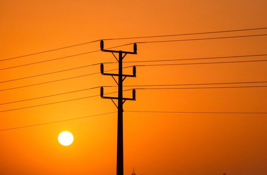 Stromleitungen vor orangefarbenem Himmel als Symbol für Stromausfall und Hitze